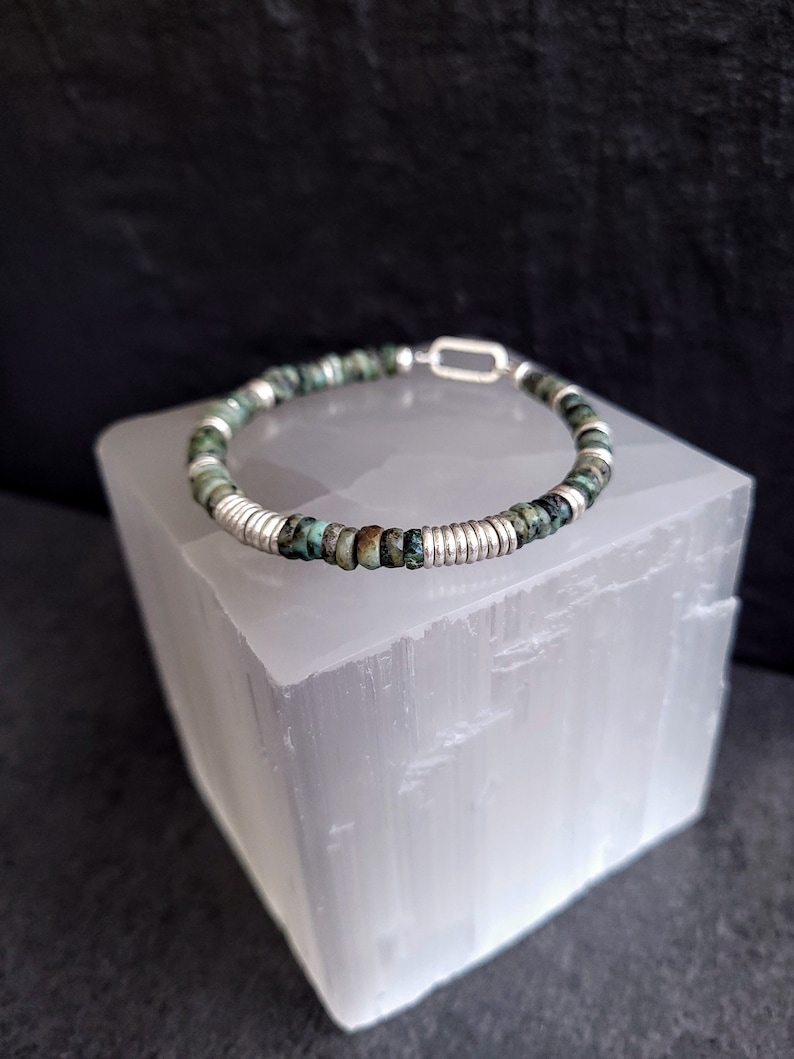 May include: A turquoise and silver beaded bracelet with a silver clasp. The bracelet is on a white selenite crystal.