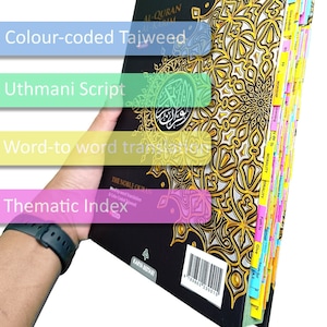 May include: A black and gold Quran with color-coded Tajweed, Uthmani Script, word-to-word translation, and a thematic index. The book has a decorative gold pattern and labeled tabs for easy navigation. The text "The Noble Quran" is visible.