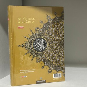 May include: A gold-colored book with an intricate design on the cover. The title is "Al-Quran Al-Karim" in English. The book is a translation of the Quran with word-by-word translation and color-coded Tajweed. The size is A5 Small.