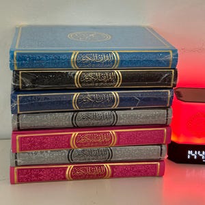 May include: A stack of eight blue, black, and pink hardcover books with gold lettering and intricate designs on the covers. The books are all the same size and are stacked neatly on a table.