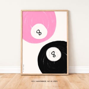 Pode incluir: Impressão de arte abstrata com duas bolas oito estilizadas. Uma é rosa, a outra preta, ambas com um círculo branco e o número oito. A obra de arte é emoldurada em uma moldura de madeira clara sobre um fundo branco. O texto "100% HANDMADE. NO AI USED." está na parte inferior.