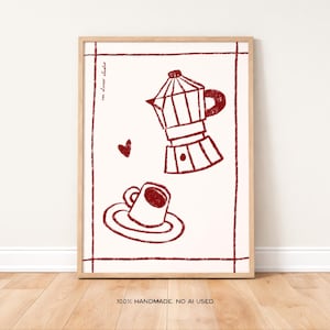 May include: Framed print with a red coffee pot, cup and saucer, and a heart on a cream background. The words "im decor studio" are in the upper left corner. The text "100% HANDMADE. NO AI USED." is in the lower right corner.