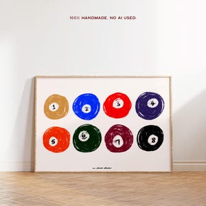 Puede incluir: Un cuadro enmarcado con ocho bolas de billar de colores, cada una con un número diferente. Las bolas están dispuestas en dos filas de cuatro, sobre un fondo blanco. El texto "100% HANDMADE. NO AI USED." está en la parte superior.