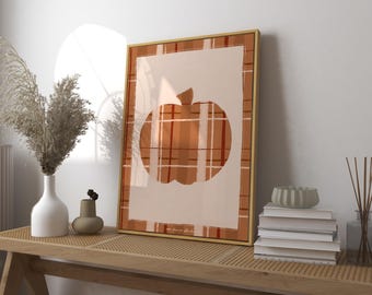 May include: A framed art print featuring a pumpkin design. The pumpkin is a warm orange color with a plaid pattern, set against a cream background. The frame is gold, and the artwork is displayed on a wooden bench with decorative items.
