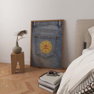 May include: A framed print showing a close-up of a denim jeans pocket. The pocket has a yellow patch with the text "lost without my trinkets" and red star accents. The frame is a warm brown colour.