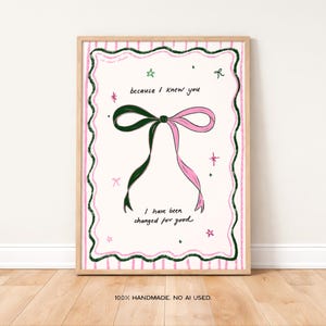 Könnte beinhalten: Ein gerahmter Kunstdruck mit einer Illustration einer grünen und rosa Schleife und dem Text "because I knew you, I have been changed for good." Das Kunstwerk hat einen rosa und grünen Rand auf cremefarbenem Hintergrund. Der Rahmen ist aus Holz.