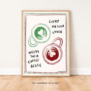 Könnte beinhalten: Ein gerahmter Kunstdruck mit cremefarbenem Hintergrund zeigt zwei Kaffeetassen-Illustrationen, eine grüne und eine rote. Die grüne Tasse hat ein Herzdesign. Der Text lautet: "EVERY MATCHA LOVER NEEDS THEIR COFFEE BESTIE".