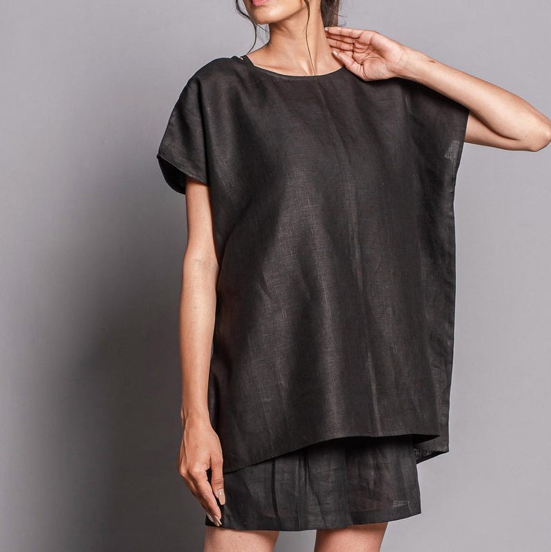 May include: A black linen tunic top with short sleeves and a round neckline. The top is loose-fitting and falls to the mid-thigh.
