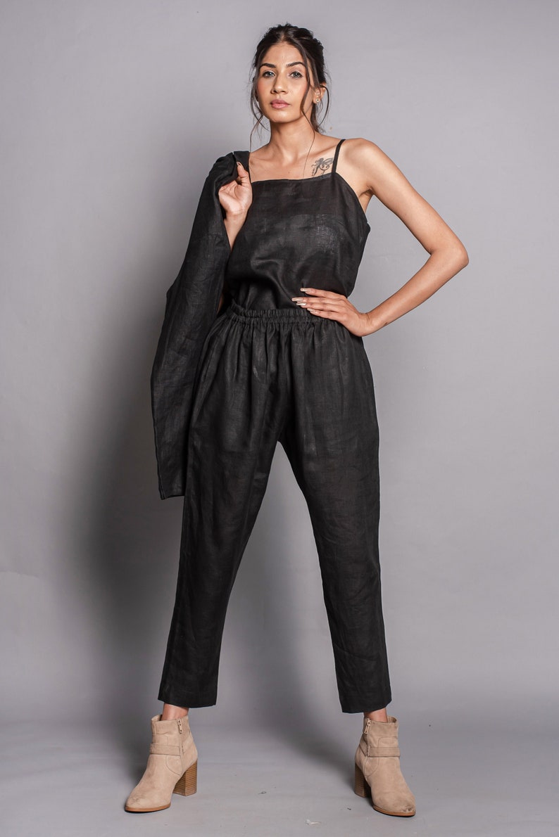 May include: A black sleeveless top with thin straps and matching black trousers featuring an elastic waistband. A black jacket is draped over one shoulder. The outfit is paired with tan suede ankle boots with a side zipper and a block heel.