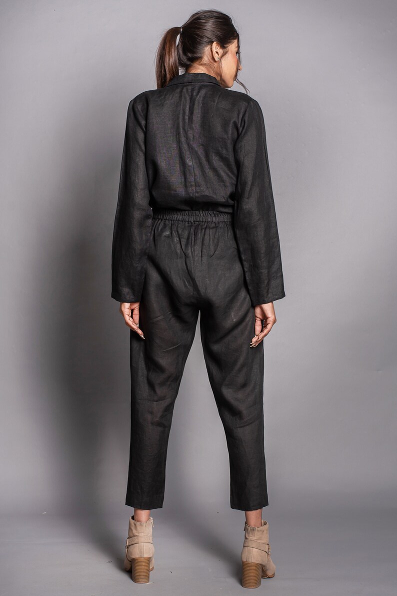 May include: A black long-sleeved jumpsuit featuring a collared neckline, a button-down front, and an elasticized waistband. The garment has tapered pant legs that end above the ankle, paired with beige ankle boots with a block heel.