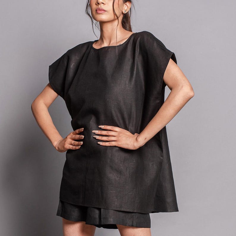 May include: A black linen top with short sleeves and a loose fit. The top has a round neckline and falls to the hips.