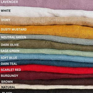May include: A stack of folded fabric swatches in various colors labeled as lavender, white, ivory, dusty mustard, neutral green, dark olive, sage green, soft blue, dark teal, scarlet red, burgundy, brown, natural, and black.