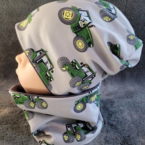 Könnte beinhalten: Graue Mütze und Halstuch-Set mit grünem Traktor-Druck. Die Mütze ist nach unten geklappt und der Halstuch ist nach oben geklappt.