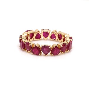 May include: A gold ring featuring heart-shaped ruby gemstones. The ring's band is made of gold and is set with a continuous row of vibrant red rubies. The gemstones are cut into heart shapes and are closely set together.