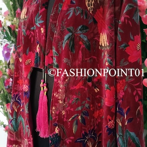 May include: A long, red velvet kimono with a floral and bird print. The kimono has pink tassels on the sleeves and at the waist.