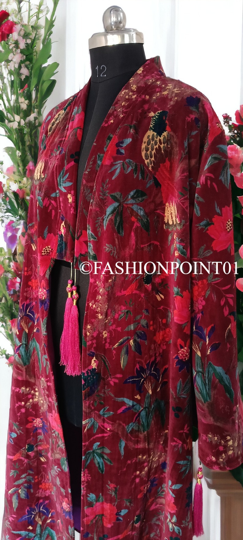 May include: A long, red velvet kimono with a floral and bird print. The kimono has pink tassels on the sleeves and at the waist.