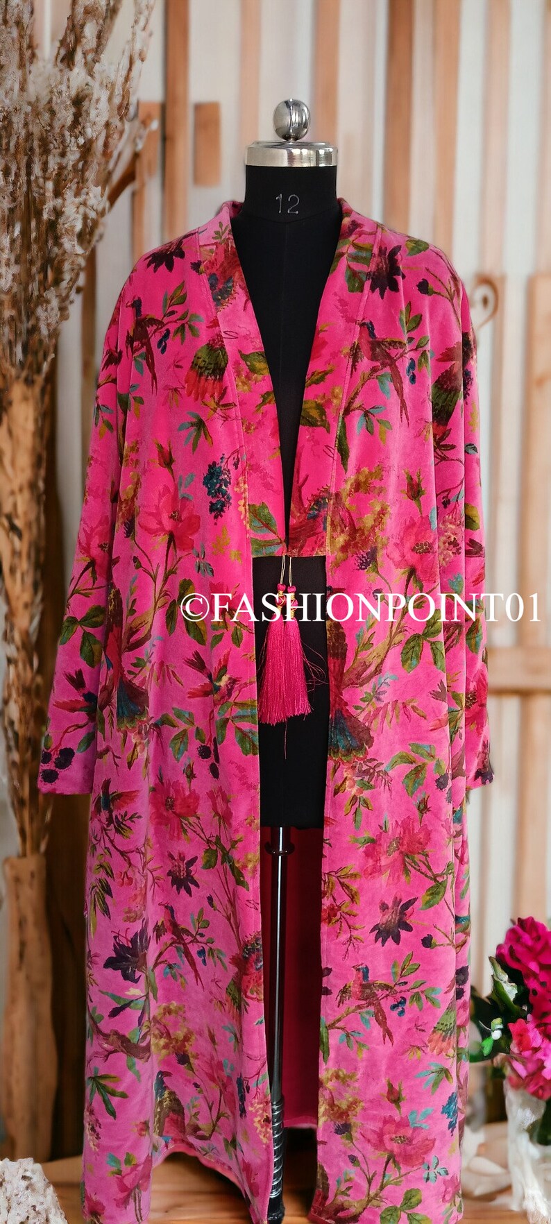 Puede incluir: Un kimono de terciopelo rosa con estampado floral y de p&aacute;jaros. El kimono tiene un cierre de borla y se muestra en un maniqu&iacute;.