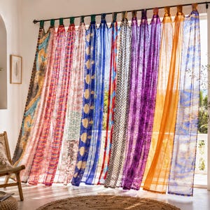 May include: A set of sheer, multi-colored curtains hanging from a dark rod. The panels feature various patterns including stripes, floral motifs, and geometric shapes in vibrant shades of blue, purple, orange, red, and yellow, allowing light.