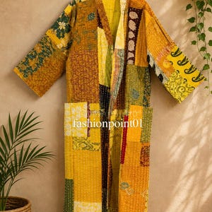 May include: A long-sleeved robe featuring a patchwork design in shades of yellow, mustard, green, and brown. The garment is constructed from quilted fabric with visible white stitching throughout and includes two front pockets. The text fashionpoint01 is visible.