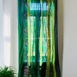 Op de afbeelding: Groene patchwork gordijnen met verschillende texturen en patronen, waaronder bloemenborduurwerk, stippen en strepen. De gordijnen hangen aan een witte muur met een raam erachter.