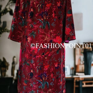 May include: A long, red velvet robe with a floral print featuring birds and flowers. The robe has a tassel on the front.