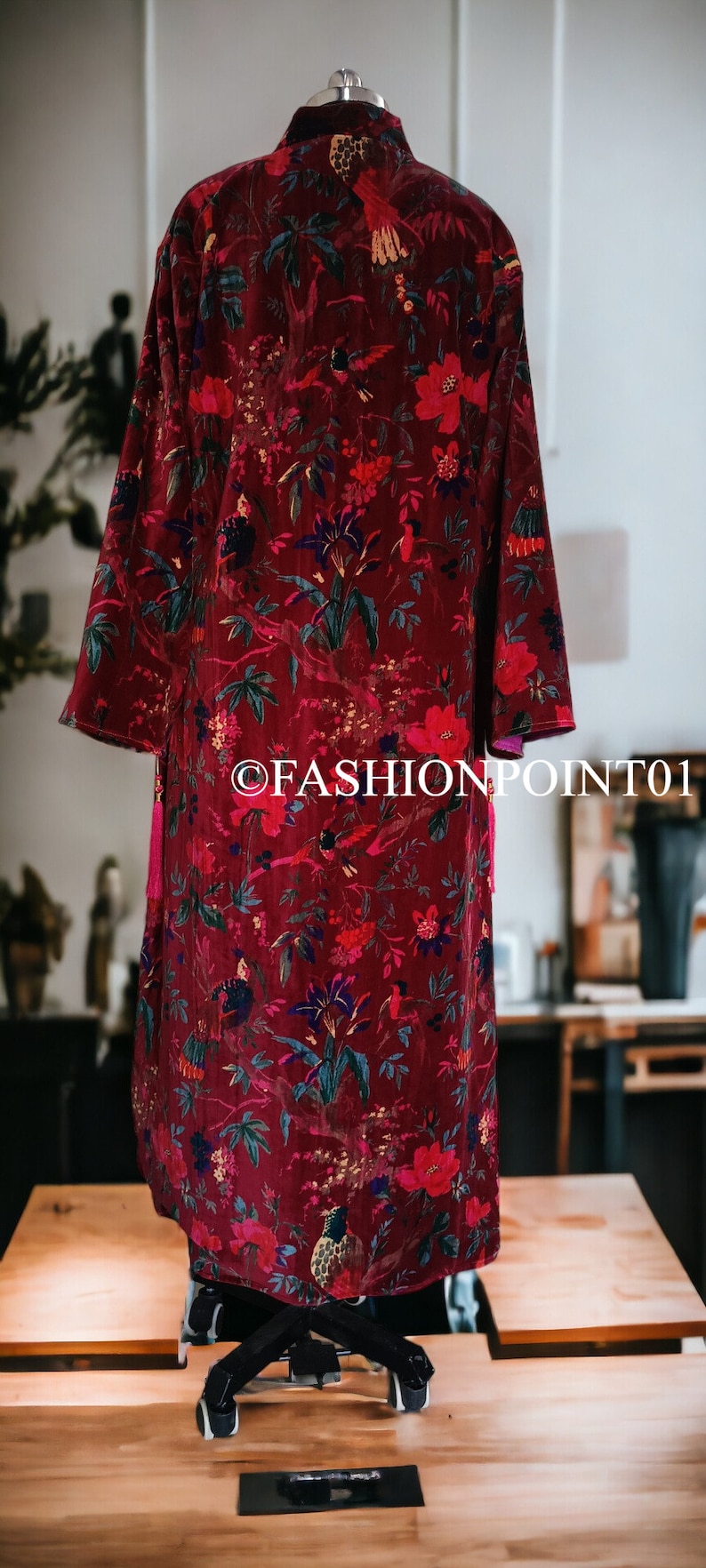 May include: A long, red velvet robe with a floral print featuring birds and flowers. The robe has a tassel on the front.