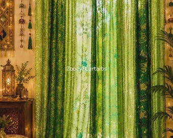 May include: Sheer green curtains featuring a variety of botanical and floral patterns in multiple shades of green, hung with tab tops and accented by a string of small tassels. The text Zooey Curtaibs is printed in the center of the fabric.