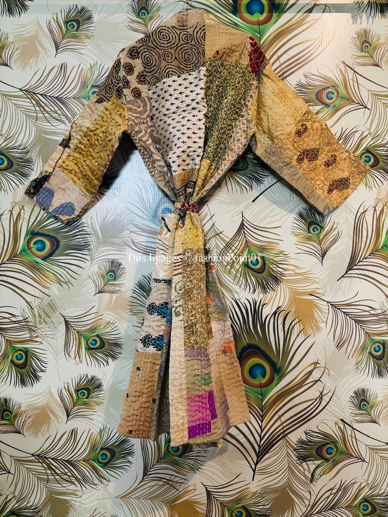 Puede incluir: Una bata de patchwork de estilo kimono con motivos en patchwork de colores marr&oacute;n, beige y verde. La bata tiene un cierre de nudo y mangas largas. La bata est&aacute; fotografiada sobre un fondo de plumas de pavo real.