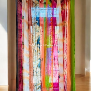 May include: A colourful patchwork curtain made of sheer fabric with a variety of patterns and colours, including pink, orange, green, blue, and white. The curtain is hung on a metal rod and is tied back with fabric ties.