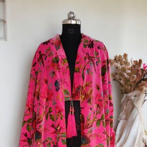 Puede incluir: Un kimono de terciopelo rosa con estampado floral y de p&aacute;jaros. El kimono tiene un cierre de borla en la parte delantera.