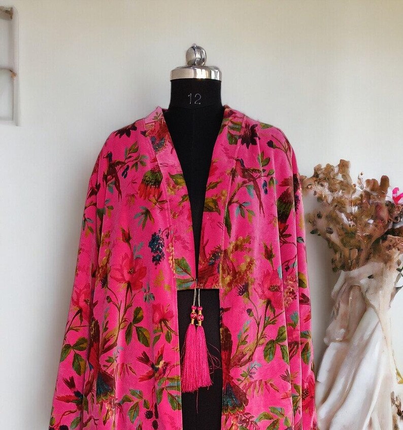 Puede incluir: Un kimono de terciopelo rosa con estampado floral y de p&aacute;jaros. El kimono tiene un cierre de borla en la parte delantera.