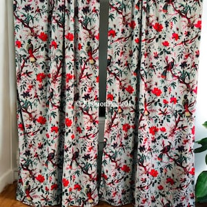 May include: A pair of gray curtains with a floral print featuring red flowers, green leaves, and colorful birds. The curtains are hung on a white wall and reach the floor.