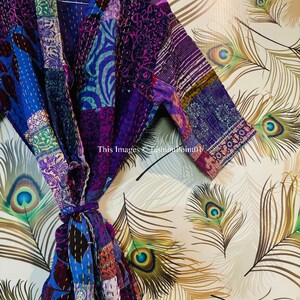 Op de afbeelding: Een patchwork kamerjas met een levendige mix van paarse, blauwe en magentakleurige stoffen panelen met ingewikkelde kantha-stiksels. Het kledingstuk heeft een sjaalkraag, driekwartmouwen en een bijpassende ceintuur. Tekst: This Images &copy;FashionPoint01.