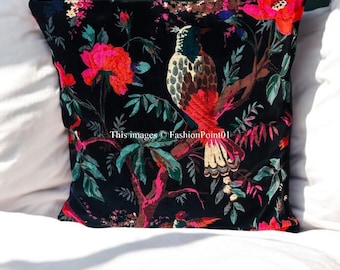 May include: A black velvet pillow with a floral and bird design. The flowers are pink, red, and white. The birds are brown, red, and green. The pillow is on a white bed.