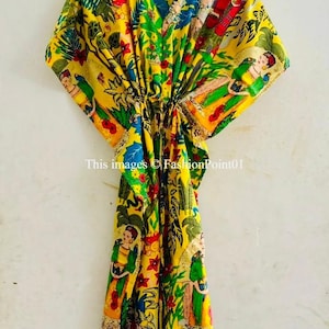 May include: Yellow kaftan with a vibrant print featuring figures, foliage, and floral elements in red, green, blue, and white. The garment has a V-neck and is hanging on a yellow hanger. The text "This images © FashionPoint01" is visible.