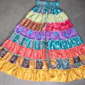 May include: Multicoloured palazzo trousers with a layered, ruffled design. The trousers are made from a variety of fabrics and feature a rainbow of colours, including yellow, orange, red, purple, blue, and green.