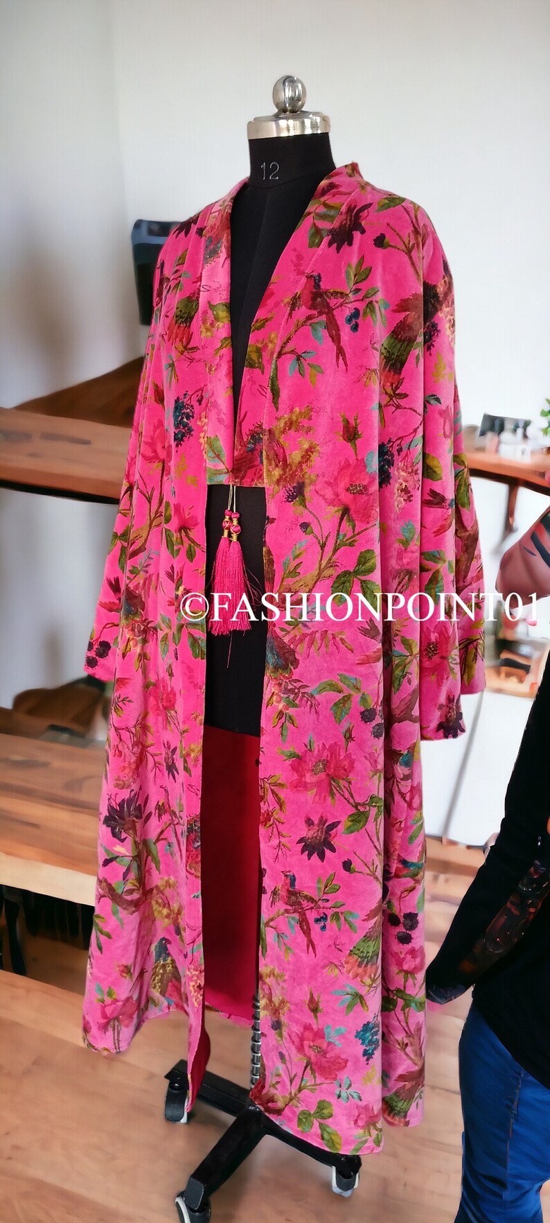 Puede incluir: Un kimono de terciopelo rosa con estampado floral que presenta p&aacute;jaros y flores. El kimono tiene una silueta larga y fluida y un detalle de borla en el escote.