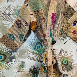 Puede incluir: Una bata de patchwork con una variedad de colores y patrones, incluyendo dise&ntilde;os florales, geom&eacute;tricos y paisley. La bata est&aacute; atada a la cintura con una cinta y tiene mangas largas. La bata est&aacute; fotografiada sobre un fondo de plumas de pavo real.