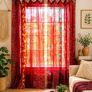 Pode incluir: Um par de cortinas que vão até ao chão com um design de patchwork de painéis de tecido vermelho, laranja e amarelo com vários padrões florais e geométricos. As cortinas estão penduradas numa barra preta usando presilhas de tecido.