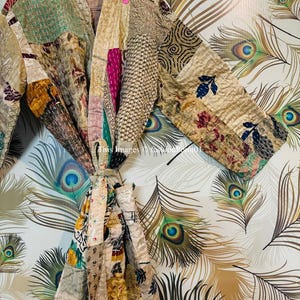 Puede incluir: Una bata de patchwork con fondo crema y coloridos patrones florales y geom&eacute;tricos. La bata se ata a la cintura con una cinta y tiene mangas largas.