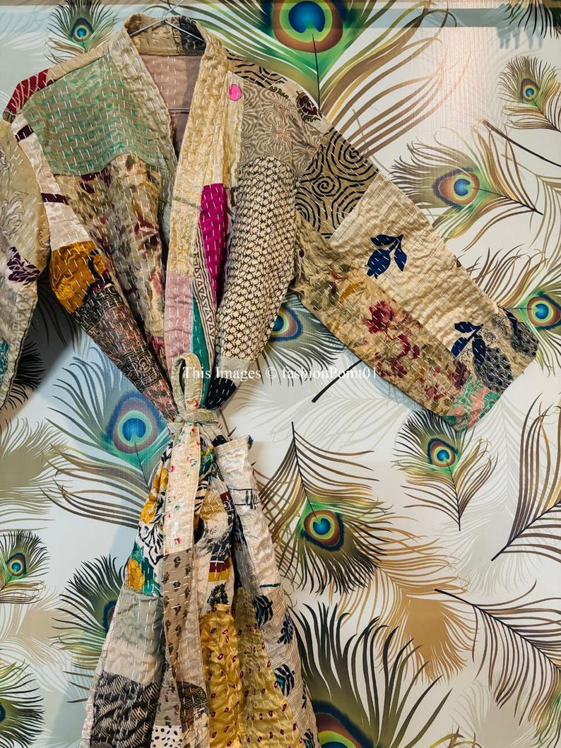Puede incluir: Una bata de patchwork con fondo crema y coloridos patrones florales y geom&eacute;tricos. La bata se ata a la cintura con una cinta y tiene mangas largas.