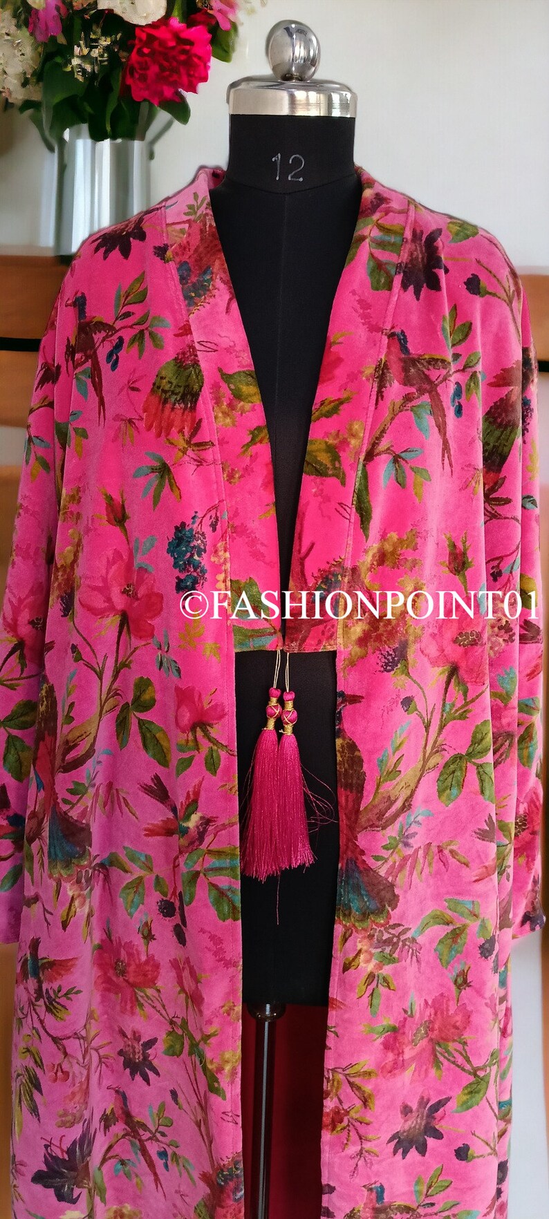 Puede incluir: Un kimono de terciopelo rosa con estampado floral y de p&aacute;jaros. El kimono tiene una abertura larga y abierta en la parte delantera y un cierre de lazo en la cintura. El kimono est&aacute; decorado con dos borlas rosas.