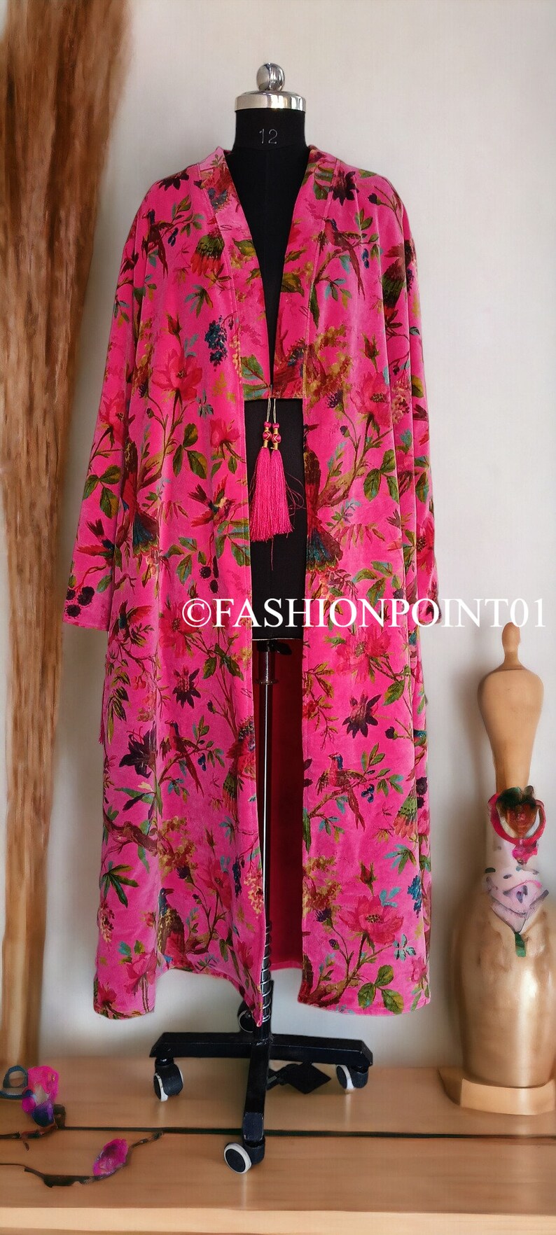 Puede incluir: Un kimono de terciopelo rosa con estampado floral y de p&aacute;jaros. El kimono tiene un detalle de borla en la parte delantera.