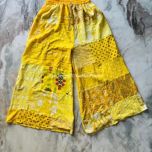 May include: Yellow palazzo trousers with a patchwork design featuring various floral and geometric patterns. The trousers have an elastic waistband and a drawstring.