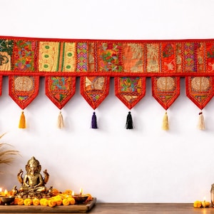 May include: A vibrant, red wall hanging with intricate patchwork designs and decorative tassels. The textile features a variety of patterns and colors, including gold, green, and blue. The hanging is adorned with multiple tassels in various colors.