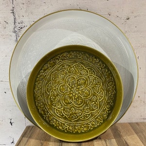 Peut inclure: Deux plateaux de service décoratifs. Un grand plateau blanc avec un bord doré et un motif floral en relief est derrière un plus petit plateau vert olive avec un motif floral en relief détaillé. Les plateaux sont sur une surface en bois.