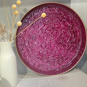 May include: A large, round, purple metal tray with an intricate embossed design. The tray has a gold rim and is perfect for serving or displaying items.