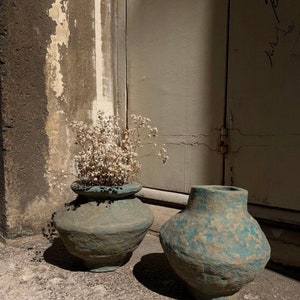 May include: Two blue ceramic vases with a rough, textured surface. One vase is filled with white dried flowers.