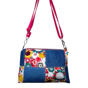 May include: A patchwork crossbody bag with a denim blue base and floral print panels. The bag has a hot pink adjustable strap and silver-tone hardware. The zip closure is visible at the top.