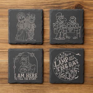 Op de afbeelding: Set van vier vierkante leistenen onderzetters met geëtste witte lijntekeningen. Ontwerpen omvatten Muppet-personages en citaten: "I AM HERE TO TELL THE STORY" en "Light the LAMP NOT THE RAT". Elke onderzetter is ongeveer 10 cm vierkant.